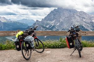 Two touring bicycles with luggage parked against a scenic mountain backdrop under cloudy skies.
