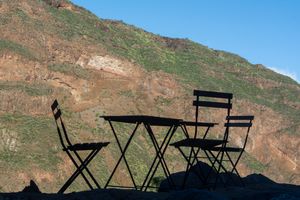 Silhouette of a bistro table and chairs against a rocky mountain backdrop.
